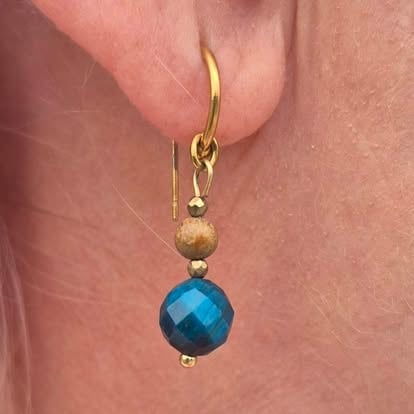 Gold drop earring with faceted blue stone and small metallic bead on womans ear